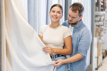 Fototapeta premium Husband and wife choose beautiful curtains for the windows of their new home together