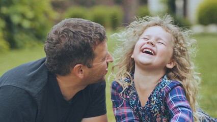 Father laughing together with daughter during sunny park walk, enjoying playful bonding moment with...