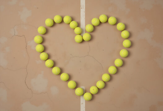 Yellow tennis balls are creatively arranged to form a heart shape on a cracked tennis court. The setting highlights a playful and artistic take on sports during daytime - Powered by Adobe
