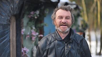 Homeless man with warm smile standing near improvised shelter, revealing human dignity within...