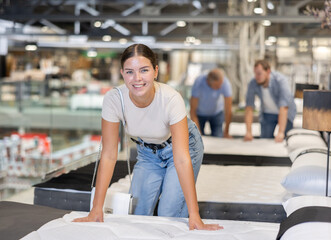 Happy young woman is testing mattress on bed in the store