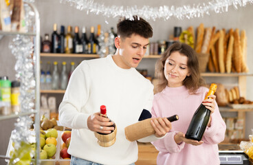 Couple of young men and women choosing wine in store decorated for new year