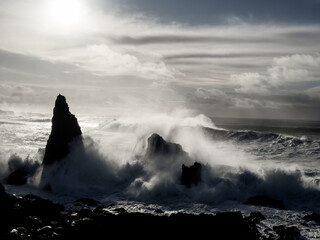 Massive waves crash against the rugged sea stacks of Valahnúkamöl as sunlight filters through the mist. A dramatic seascape showcasing Iceland’s raw and untamed coastal beauty