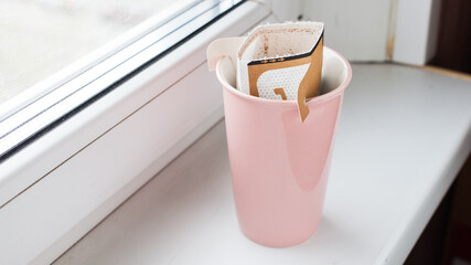 Drip bag in a ceramic cup on windowsill. Instant freshly brewed alternative filter drink in mug. Easy brew black coffee method for home, travel or office. cozy trendy lifestyle