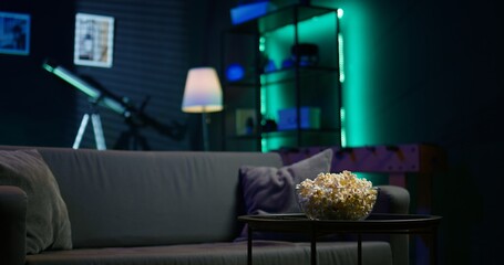 Apartment room with dimmed lighting, popcorn and remote on small table, creating relaxed mood for...