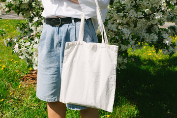 Woman hand holding eco bag. Female hold white canvas textille mesh zero waste shopper on city...