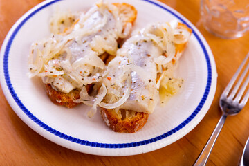 Appetizing sandwich with marinated herring and onions served on plate in restaurant