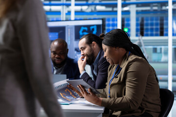 Photovoltaics factory management executives using tablet look over schematics, upgrading facility floor. African american solar panels plant manager holding device looks over assembly lines blueprints