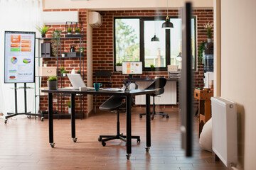 Vacant brick wall room with organized digital devices and furniture prepared for employees to use. Startup company workspace is well arranged with computers and modern office materials.