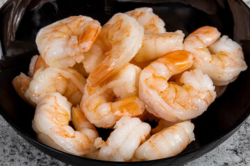A black dish of cooked peeled shrimp without tails on a grey table