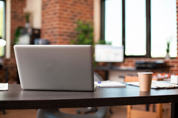 Startup office neatly prepared for meetings and research, having vacant desk with essential work items like laptop and papers. Table with digital device, coffee cup, and documents, ready for busy day.
