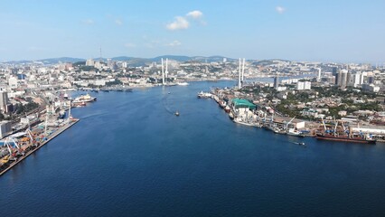 Obraz premium Aerial panorama capturing vladivostok's zolotoy rog bay, featuring industrial vessels, cable stayed zolotoy bridge gleaming under bright sunlight