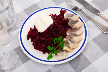Pieces of chopped herring with grounded beetroot served on plate. Fish refreshment on table.