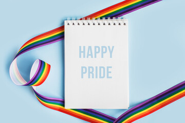 Obraz premium LGBT raibow flag ribbon with notebook or note mock up on light blue background. Flat lay, top view, trendy minimal composition, concept of gay pride of proud month lgbtq community. Cultural divesity
