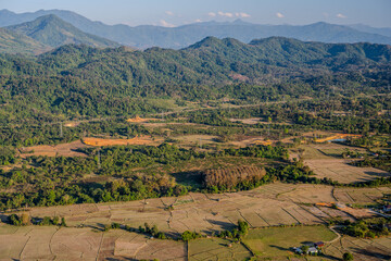 Fototapeta premium Aerial Landscape of Harvested Rice Fields and Lush Green Hills in the Rural Outskirts of Vang Vieng, Laos During Golden Hour