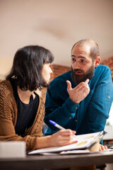 Fototapeta premium Closeup on businessman and woman with clipboard discussing about startup company revenues. Young male and female colleagues at office desk, reviewing and brainstorming financial strategy ideas.
