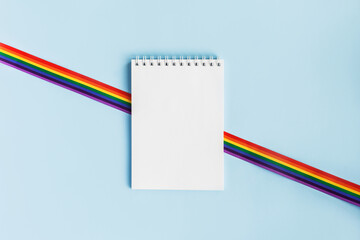 LGBT raibow flag ribbon with notebook or note mock up on light blue background. Flat lay, top view,...