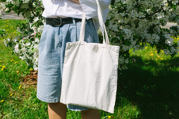 Woman hand holding eco bag. Female hold white canvas textille mesh zero waste shopper on city...