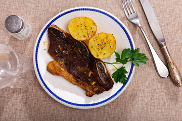 Delicious churrasco style grilled veal ribs served on plate with side dish of spicy baked potatoes garnished with fresh parsley