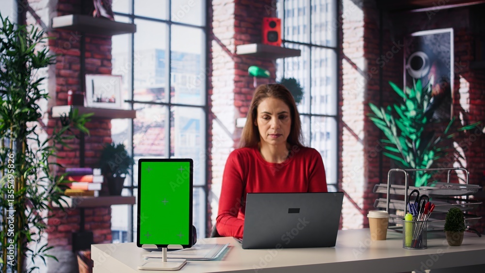Poster confident woman solving tasks on a freelance platform next to mockup screen, answering emails and mu