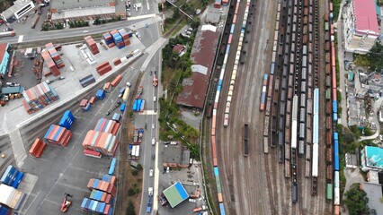 Aerial panorama revealing sprawling freight terminal with parked trains, multicolored containers, bustling transport vehicles
