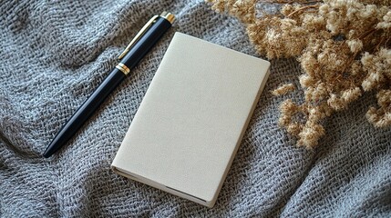 Fototapeta premium Blank notebook, pen, and dried flowers on textured fabric.