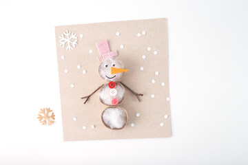 Handmade snowman craft made of natural materials on beige cardboard background. Flat lay...