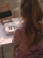Girl in pink dress playing keyboard during online session back view.