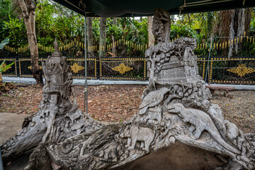 Intricately carved wooden sculptures depicting animals, temples, and landscapes under canopy in a Buddhist temple garden in Vientiane, Laos