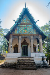 Fototapeta premium Ancient Buddhist Temple with Ornate Mosaic Façade and Traditional Architecture at Wat Tham Phou Si in Luang Prabang, Laos