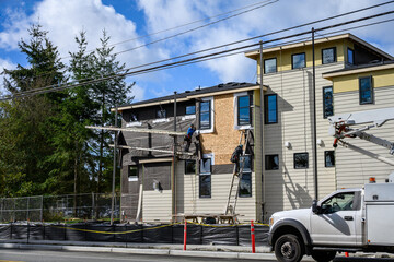 New housing development home construction, workmen on scaffolding and ladder installing moisture...