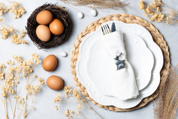 Easter table setting with white plates, napkin, and nest with eggs. Decorated with dried flowers...