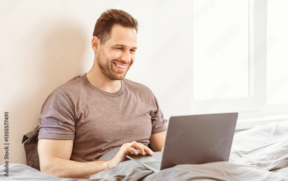Poster work from home. cheerful guy using laptop computer working online remotely sitting in bed indoors. f