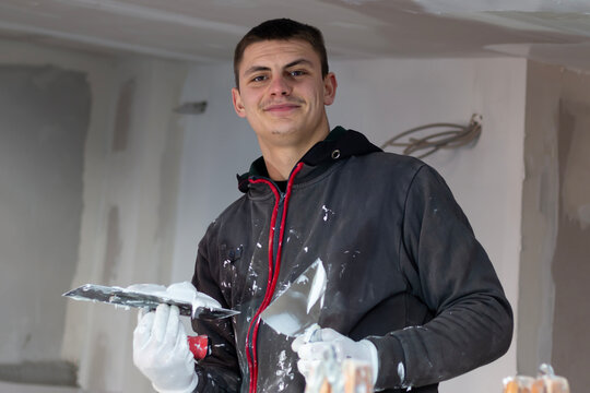 A young builder worker spackling ceiling with putty plaster aligning ceiling with spatula. Renovation and construction works. House improvements.