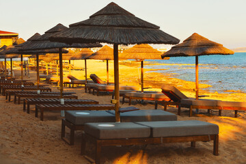 Sandy beach glows under the sun, dotted with rustic straw umbrellas. Waves whisper softly, inviting you to relax in the serene, tropical paradise