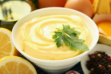 Delicious mayonnaise sauce with parsley in bowl and ingredients on table, closeup