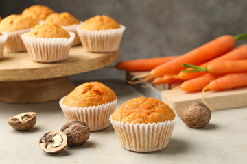 Tasty carrot muffins, fresh vegetables and walnuts on light grey table, closeup
