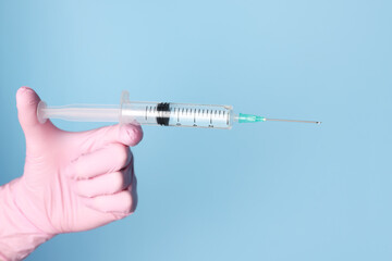 Doctor holding syringe with medication on dusty light blue background, closeup