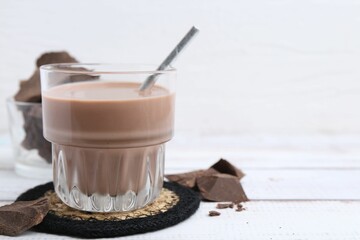Tasty chocolate milk in glass and pieces of chocolate on white wooden table, closeup. Space for text