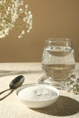 Collagen powder in bowl, spoon, glass of water and gypsophila branches on light textured table...