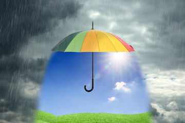 Sun shining over green meadow under open colorful umbrella during heavy rain
