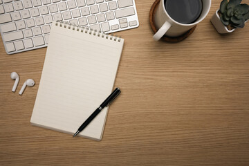 Minimalist workspace with notebook and coffee cup and wireless earbuds on wooden desk