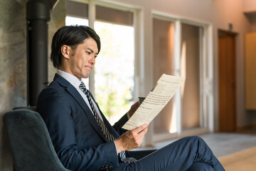 朝家やホテルで英字新聞を読むスーツ姿のアジア人ビジネスマン

