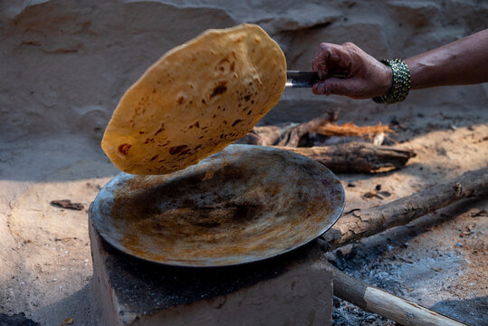 A village woman makes bread on the stove. cooking bread in clay stove , chula , makeing bread , roti , in village