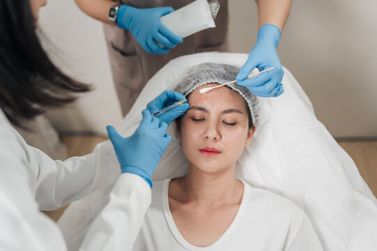 Medical experts in white coats carefully perform the procedure. Asian woman receiving a professional beauty injection on her forehead. Anti-aging beauty treatment at a modern aesthetic clinic.
