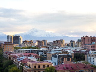 Fototapeta premium Scene of Yerevan cityscape with buildings and trees, with Mount Ararat on sky and clouds background, high view from Yerevan cascade, a modern architecture building complex at Yerevan, Armenia.