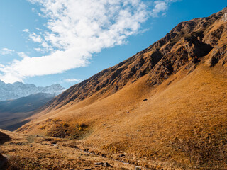 Dirt path as hiking route between beautiful complex hills on autumn season mountains background, walking view at Georgia. Brown and yellow grass on small mountain, beauty landscape.