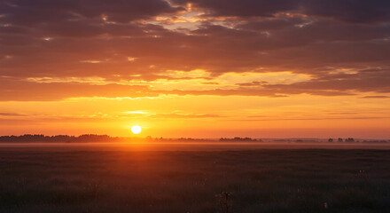A bright sunrise over a field with cloudy orange sky