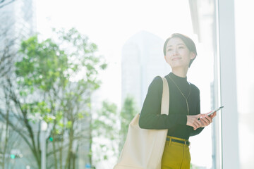 オフィス街をスマートフォンを見ながら歩く30代日本人女性