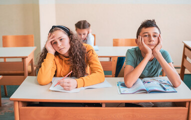 Tired and bored child students sitting in a school desk during the class.
